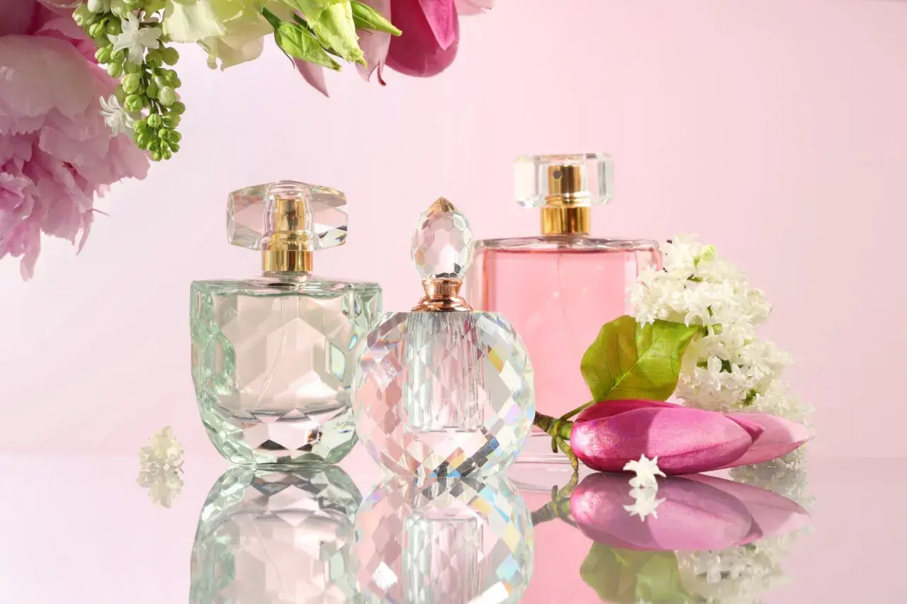 Eleganckie flakony z wodą toaletową lub perfumowaną, otoczone kwiatami.